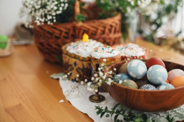 Paskalya yumurtaları ev yapımı paskalya pastası, mum, yeşil dallar ve ahşap masa üzerinde sepetli çiçekler üzerine doğal boyanmış. Kutsamak için Paskalya Yemeği