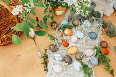 Sepeti, mumu, bahar çiçekleri ve yeşil dalları olan paskalya yumurtaları. Modern süslemelerle doğal boyayla boyanmış renkli Paskalya yumurtaları. Kırsal düzlük