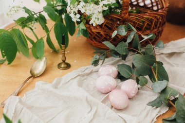 Okaliptüs dallı modern Paskalya yumurtaları sepet ve mumlu ahşap masa üzerinde. Paskalya yumurtaları pancardan doğal boya ile boyanmış. Mutlu Paskalyalar