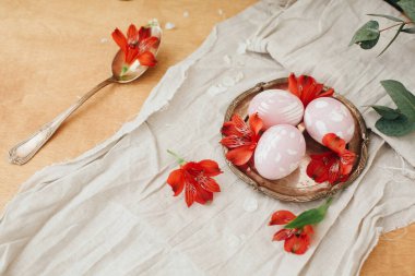 Çarşaf bezinde kırmızı çiçekli modern Paskalya yumurtaları ve kırsal ahşap masadaki taçyapraklı kaşıklar. Paskalya yumurtaları pancardan doğal boya ile boyanmış. Mutlu Paskalyalar