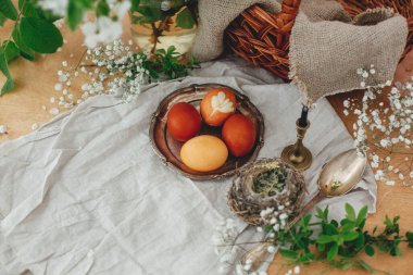 İlkbahar çiçekleri, mum ve sepetli kırsal masada antika tabakta modern Paskalya yumurtaları. Şık kırmızı ve sarı Paskalya yumurtaları soğan ve zerdeçal boyasıyla boyanmış. Mutlu Paskalyalar