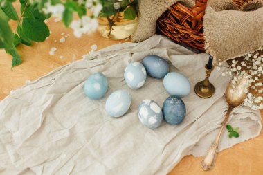 Çağdaş Paskalya yumurtaları kır masasında bahar çiçekleri, sepet, keten kumaş. Kırmızı lahanadan doğal boyayla boyanmış mavi paskalya yumurtaları. Mutlu Paskalyalar. Kırsal yaşam