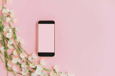 Pembe akıllı telefon, boş ekran ve pembe düz yatağında beyaz bahar çiçekleri. Çiçek ihalesi kenarı ve kopyalama alanı olan telefon şablonu. Zarif kız tebrik kartı. Mutlu kadınlar günü ya da anneler günü