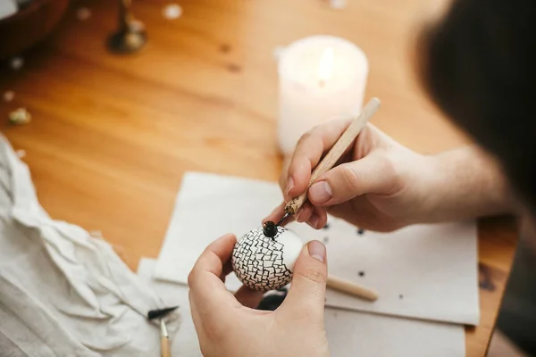 stock image Hands painting easter egg with hot wax on background of wooden table. Modern Easter eggs with stylish wax ornaments. Happy Easter. Zero waste. Ukrainian traditional egg pysanka