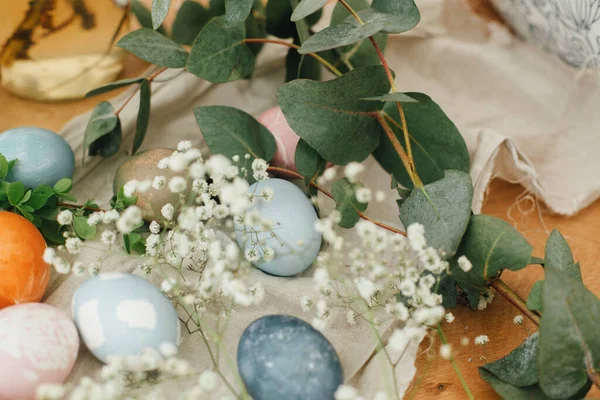 Easter eggs with modern minimal ornaments painted with natural dye on rustic background. Stylish colorful Easter eggs on wooden table with spring flowers and green branches. Zero waste holiday