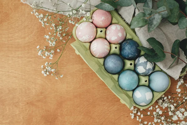 Easter eggs natural dye in carton tray on rustic table with flowers, flat lay. Modern pastel pink and blue easter eggs painted with organic beets, red cabbage, carcade tea. Zero waste holiday
