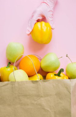 Pembe eldiveni ver. Sarı biberi pakete koy. Pembe arka planda paketler olsun. Karantinada güvenli alışveriş. İnternetten yemek sipariş et ve evde kal. Virüsün önlenmesi