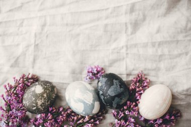 Kırsal keten kumaş ve mor leylak çiçekli modern Paskalya yumurtaları. Kırsal yaşam. Mutlu Paskalyalar. Mesaj için yer var. Doğal boyalı paskalya yumurtaları. Güzel bir bayram tebrik kartı.