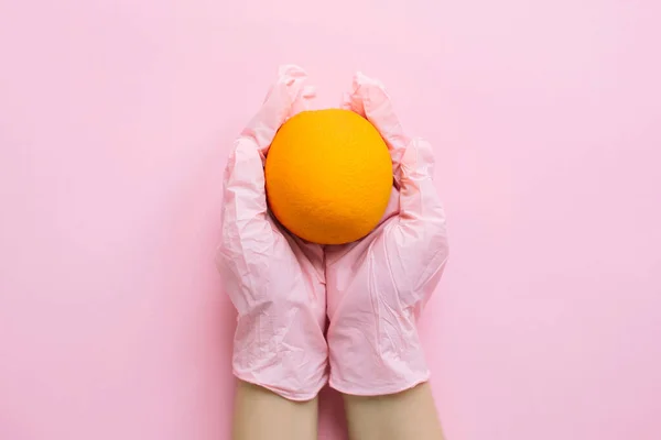 Manos Guante Rosa Sosteniendo Naranja Sobre Fondo Rosa Plano Laico —  Fotos de Stock