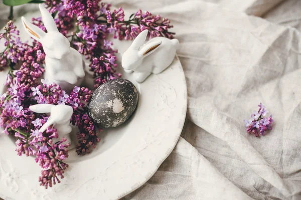 复活节快乐时尚的复活节白兔 老式盘子上的现代复活节彩蛋和亚麻布乡村织物上的丁香花 天然染色的复活节彩蛋和春花 案文的篇幅 — 图库照片