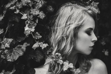 Avrupa caddesinde yeşil sarmaşık yaprakları altında şık bir kadın portresi. Modaya uygun bir kadın yeşil yaprakların altında poz veriyor. Sokakta eski ahşap bir kapının arkasında.