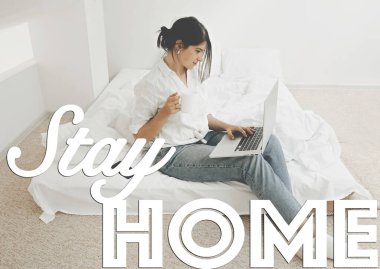 Evde kalıp mesaj at. Beyaz yatakta dizüstü bilgisayarı ve elinde kahveyle oturan mutlu, şık bir kız. Evde kal, hayat kurtar. Salgını önlemek için evde izolasyon