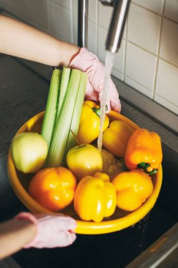 Sebze yıkıyorum. Pembe eldivenli eller lavabodaki su deresinin altında sarı kasede sebze yıkıyor. Kadın taze biber, kereviz, karnabahar temizliyor, yemek pişirmeye hazırlanıyor.