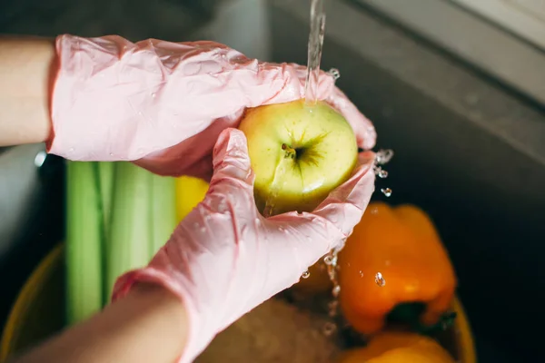 洗水果 在病毒流行期间 手戴粉色手套 在水里洗苹果 在水池里洗苹果 妇女清洁新鲜蔬菜和水果 准备在现代厨房做饭 — 图库照片