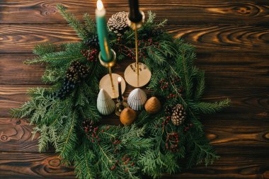 Mutlu noeller. Yılbaşı ağaçları ve mumlar koyu renkli ağaçların üzerinde Noel çelengi. Şenlikli modern dekor. Minyatür çam ağaçları, şamdan ve böğürtlen ve kozalaklı modern çelenk.