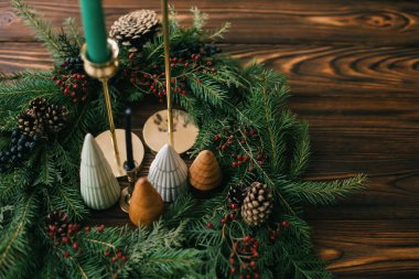 Yılbaşı ağaçları ve mumlar koyu renkli ağaçların üzerinde Noel çelengi. Şenlikli modern dekor. İyi tatiller. Minyatür çam ağaçları, şamdan ve böğürtlen ve kozalaklı modern çelenk.