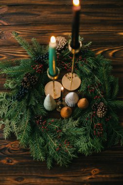 Yılbaşı ağaçları ve mumlar koyu renkli ağaçların üzerinde Noel çelengi. Şenlikli modern dekor. İyi tatiller. Minyatür çam ağaçları, şamdan ve böğürtlen ve kozalaklı modern çelenk.