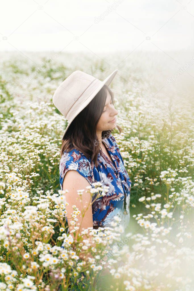 Sensual portrait of young woman in blue vintage dress and hat relaxing in summer meadow in many white wildflowers. Tranquil summer in countryside