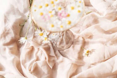 Güneşli ışıkta yumuşak bej kumaşın arka planında şarap kadehinde papatya çiçekleri. Yumuşak çiçekli estetik. Yaratıcı yaz imajı. Bohem havası.