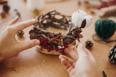 Çiçekçi, kır yılbaşı mum tutacağı yapıyor. Çam kozalakları, dallar, anason ve ahşap masa üzerinde sade şenlik dekorasyonu yapan eller. Tatil atölyesi