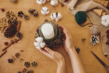 Kırsal Noel mum tutacağı dekoru yapıyorum. Düz yatıyordu. Elleri ahşap masada pamuklu, dallı, kozalaklı, anason ve makaslı sade mum tutuyordu. Tatil atölyesi