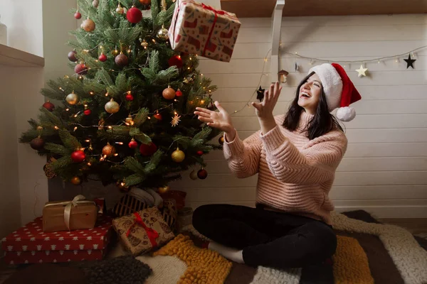 Стильная Молодая Женщина Бросает Рождественскую Подарочную Коробку Улыбается Елкой Огнями — стоковое фото