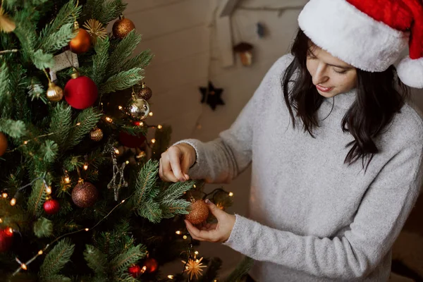 Стильная Молодая Женщина Шляпе Санты Украшает Рождественскую Елку Блестящим Золотым — стоковое фото
