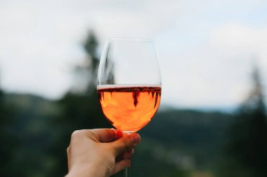 Dağların arka planında, yaz tatilinde ve tatil beldesinde Aperol içeceği. Lezzetli turuncu kokteyl ile tezahürat yapan kadın, dışarıda kutlama yapan.