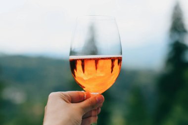 Dağların, yaz tatilinin ve tatil beldesinin arka planında lezzetli bir portakal kokteyli. Kadın aperol içkisiyle tezahürat yapıyor, dışarıda kutlama yapıyor.