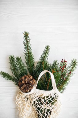 Yeşil ladin dalları ve beyaz kırsal arka planda çam kozalakları olan yeniden kullanılabilir pamuk çanta. Kış dekorasyonlu ağ alışveriş torbası, sıfır ziyan tatili. Metin için boşluk olan üst görünüm
