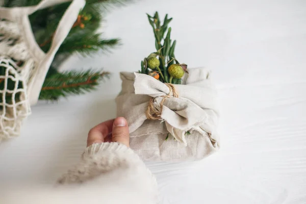 Mão Segurando Presente Natal Elegante Envolto Tecido Linho Com Ramo — Fotografia de Stock