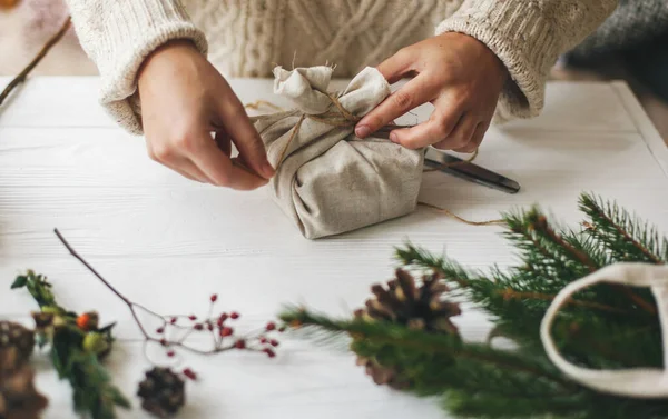 여자들은 손으로 아름다운 크리스마스 선물을 솔방울 서랍장에 아마포로 감는다 스웨터를 — 스톡 사진