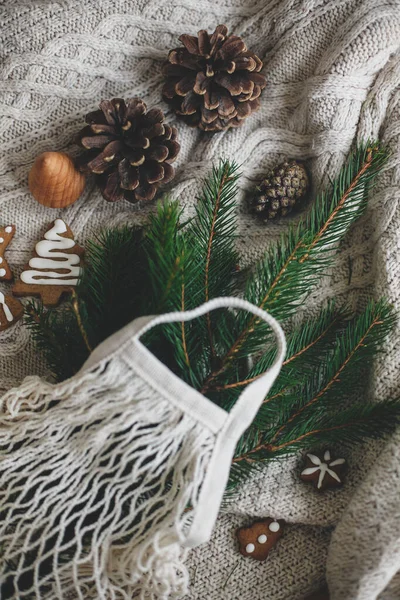 Sıfır noel ziyanı. Yeşil ladin dalları, zencefilli noel kurabiyeleri ve beyaz örgü süveter üzerinde çam kozalakları olan yeniden kullanılabilir alışveriş torbası. Plastiksiz kış süslemeleri