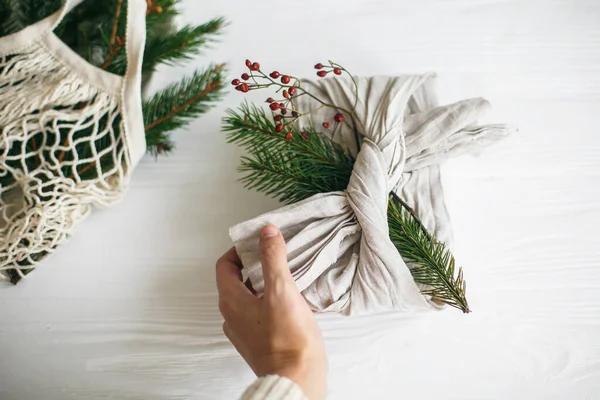 Mano Sosteniendo Elegante Regalo Navidad Envuelto Tela Lino Con Rama —  Fotos de Stock