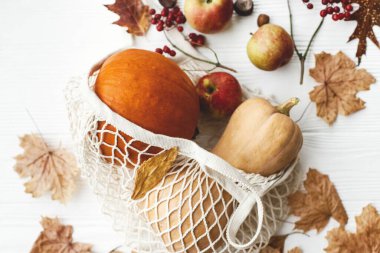 Beyaz ahşap arka planda balkabakları, elmalar, böğürtlenler, fındıklar ve sonbahar yapraklarıyla yeniden kullanılabilir alışveriş torbası. Çevre dostu Şükran Günü. Sıfır kayıp bayram, sonbahar hasat