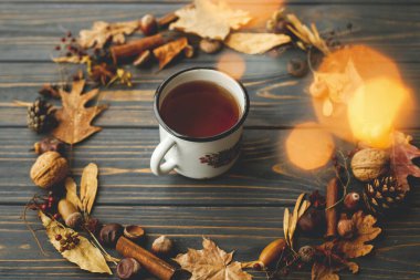 Çay ve yapraklardan, meyvelerden, meşe palamudlarından ve koyu ahşap arka planda çam kozalaklarından yapılmış sonbahar çelenkleriyle dolu Rustik metal bardak. Merhaba sonbahar! Samimi sonbahar görüntüsü