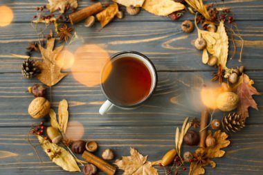 Çay ve yapraklardan, meyvelerden, meşe palamudlarından ve koyu ahşap arka planda çam kozalaklarından yapılmış sonbahar çelenkleriyle dolu Rustik metal bardak. Merhaba sonbahar! Sıcak sonbahar yatağı.