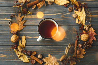 Merhaba sonbahar! Sıcak sonbahar yatağı. Çayı ve sonbahar çelengi olan, yapraklardan, meyvelerden, meşe palamudlarından ve koyu ahşap arka planda çam kozalaklarından yapılmış rostal metal bardak..