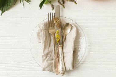 Çevre dostu Şükran Günü ziyafeti. Çatal bıçak takımı ve sonbahar süslemeleri, balkabağı, doğal dallar ve beyaz masa üzerinde sonbahar çiçekleri olan şık bir tabak. Kırsal tablo ayarı dekor