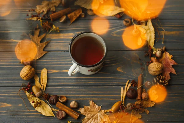 Çay ve yapraklardan, meyvelerden, meşe palamudlarından ve koyu ahşap arka planda çam kozalaklarından yapılmış sonbahar çelenkleriyle dolu Rustik metal bardak. Merhaba sonbahar! Samimi sonbahar görüntüsü