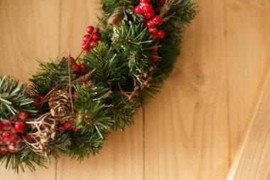 Evdeki rustik ahşap kapıya asılı Noel çelengi. Kırmızı böğürtlen ve süslemeli geleneksel Noel çelengi, çam kozalakları ve ahşap arka planda tarçın, bayram dekoru..