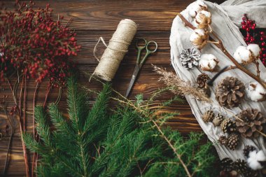 Yılbaşı ağacı dalları ve evde kırsal Noel çelengi yapmak için süslemeler. Doğal köknar dalları, çam kozalakları, kırmızı böğürtlen, otlar, sicim, pamuk ve makas. Üst görünüm