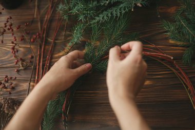 Kırsal Noel çelengi yapmak, tatil gelişimi. Kırsal ahşap arka planda yeşil köknar dalları tutan eller. Mevsimlik tatil atölyesi çevrimiçi, evde şenlikli dekorasyonlar yapılıyor.