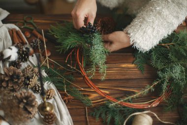 Kırsal Noel çelengi yapmak, tatil gelişimi. Kırsal ahşap arka planda yeşil sedir dalları tutan eller. Mevsimlik tatil atölyesi ya da evde şenlik dekorasyonu