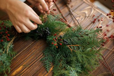 Şık, kırsal bir Noel çelengi yapmak. Elleri böğürtlen tutuyor ve kırsal ahşap arka planda doğal çelenk süslüyor. Mevsimlik tatil atölyesi ya da evde çelenk yapmak