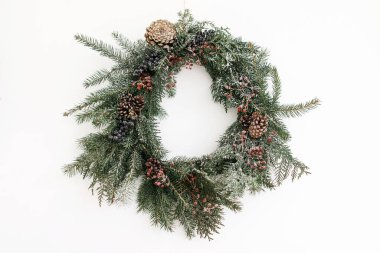 Beyaz duvarda asılı Rustik Noel çelengi, şenlikli modern dekorasyon. Kırmızı böğürtlenli ve köknar dallı yaratıcı bir Noel çelengi, beyazla izole edilmiş. Mutlu Noeller.
