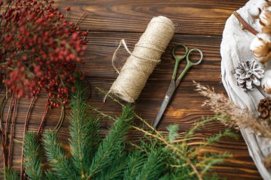 Yılbaşı ağacı dalları ve evde kırsal Noel çelengi yapmak için süslemeler. Doğal köknar dalları, çam kozalakları, kırmızı böğürtlen, otlar, sicim, pamuk ve makas. Üst görünüm