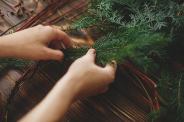 Kırsal Noel çelengi yapmak, tatil gelişimi. Kırsal ahşap arka planda yeşil köknar dalları tutan eller. Mevsimlik tatil atölyesi çevrimiçi, evde şenlikli dekorasyonlar yapılıyor.