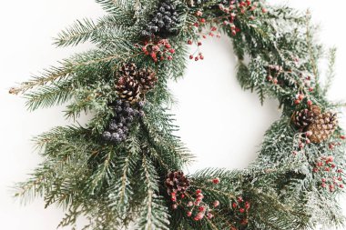 Beyaz duvarda Rustik Noel çelengi asılı, şenlikli modern dekorasyon. Kırmızı böğürtlenli ve köknar dallı yaratıcı bir Noel çelengi, beyazla izole edilmiş. Mutlu Noeller.
