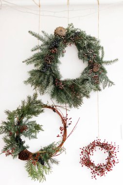 Kırmızı böğürtlenli ve köknar dallı yaratıcı doğal ve farklı noel çelenkleri, beyaza izole edilmiş. Mutlu noeller. Beyaz duvarda Rustik Noel çelengi asılı, şenlikli dekorasyon